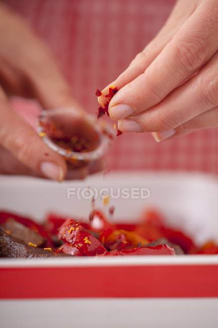 Closeup cropped view of person sprinkling chilli flakes over vegetable dish — Stock Photo
