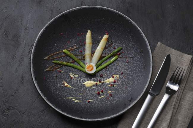 Asparagus with a quail egg on black plate  over black wooden surface — Stock Photo