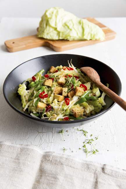 Stir-fried vegetables with tofu and pointed cabbage on black plate with wooden spoon — Stock Photo