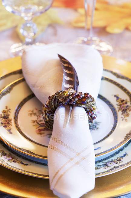 Closeup view of a festive place setting with ornate crockery and towel bundled with bracelet and feather — Stock Photo
