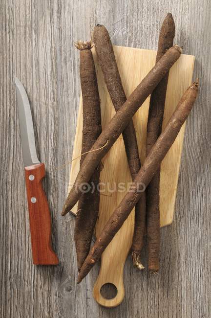 Black salsify on a chopping board next to a knife — Stock Photo
