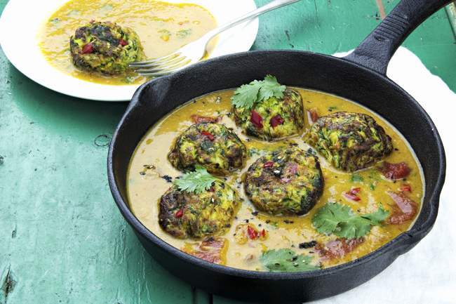 Courgette fritters in a curry sauce in pan over green surface — Stock Photo