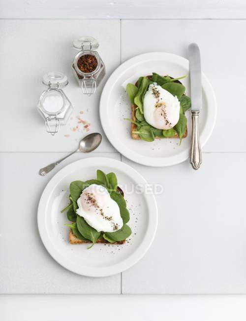 Toast mit jungem Spinat und pochiertem Ei auf weißen Tellern mit Gabel und Messer — Stockfoto