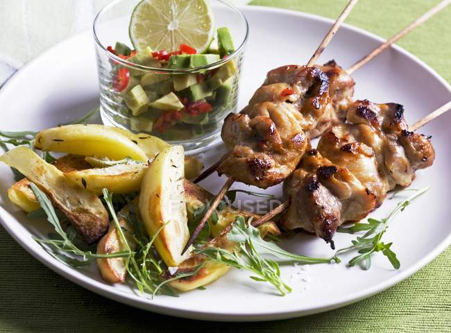Chicken kebabs with avocado salsa, potatoes and rocket on white plate — Stock Photo