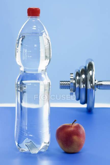 Vista close-up de garrafa de água mineral com maçã e haltere — Fotografia de Stock