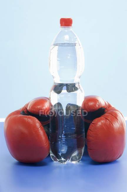 Крупный план минеральной воды в бутылке и пара боксерских перчаток — стоковое фото