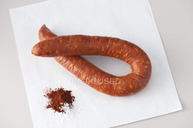 Вид крупным планом колбасы Linguica на белой бумаге с паприкой и солью — стоковое фото