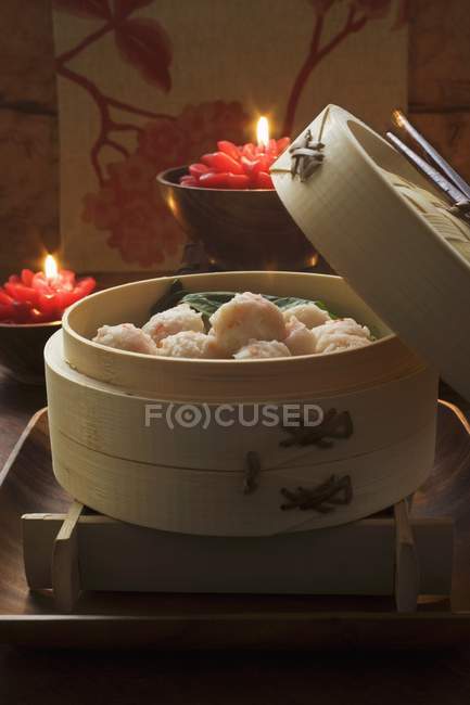 Closeup view of shrimp balls in bamboo steamer with burning candles on background — Stock Photo