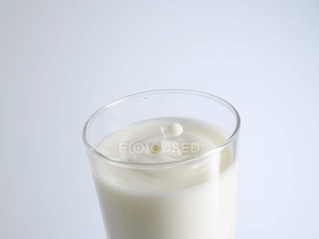 Vaso de leche con gotas de leche - foto de stock