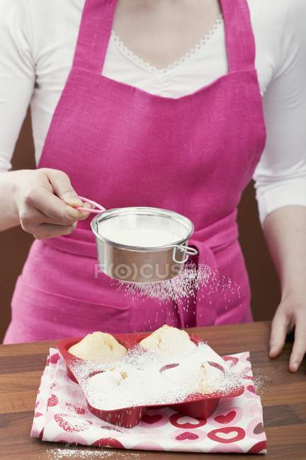 Donna spruzzando zucchero a velo sopra muffin — Foto stock