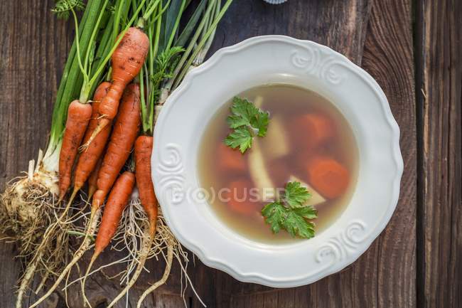 Домашний свежий овощной бульон на белой тарелке над деревянной поверхностью — стоковое фото
