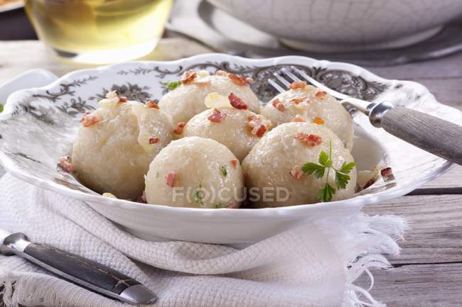 Potato dumplings with bacon on white plate over towel — Stock Photo