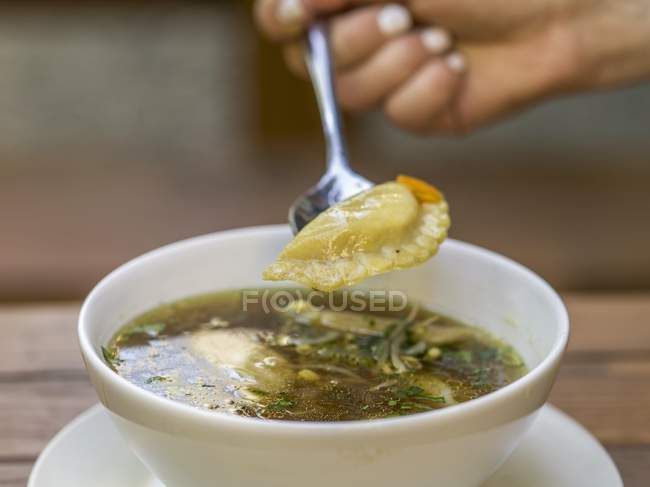Cropped view of hand holding Momo Nepalese dumpling on spoon over clear broth — Stock Photo
