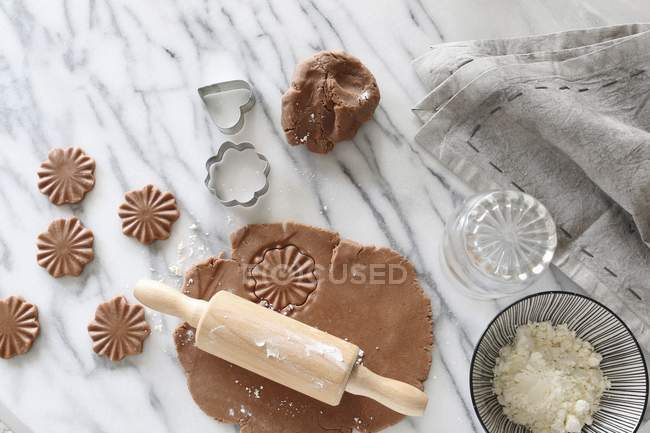 Vue de dessus de la pâtisserie sans gluten déroulée avec un rouleau à pâtisserie par des découpeuses et un bol de farine sur une surface en marbre — Photo de stock