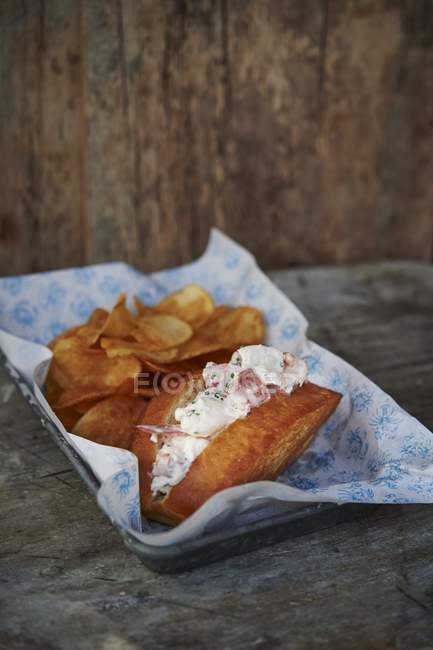 Closeup view of lobster roll with chips and sauce on paper lined dish — Stock Photo