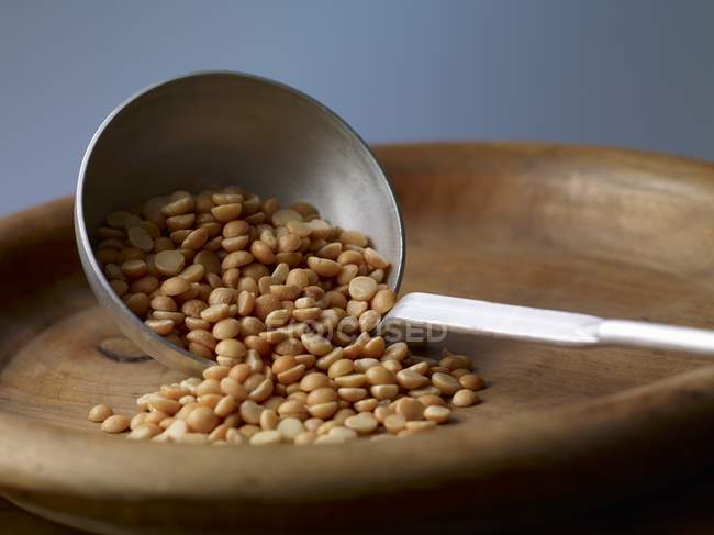 Yellow split peas on a ladle on wooden plate — Stock Photo