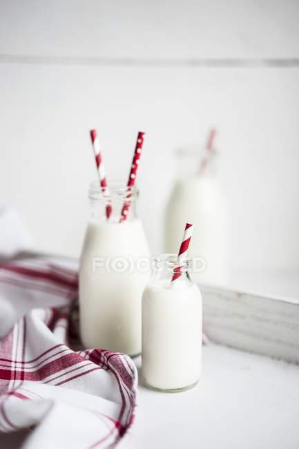 Bottles of milk with red-and-white striped straws — Stock Photo