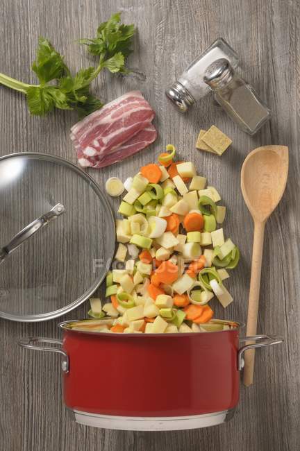 Ingredients of vegetable soup with bacon over wooden surface — Stock Photo