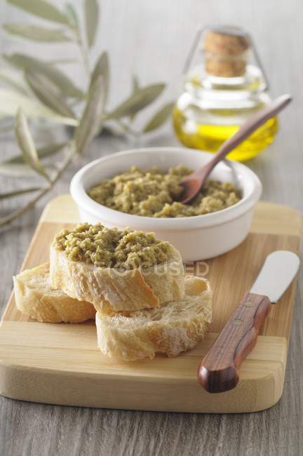 Slices of baguette with tapenade on wooden desk with knife — Stock Photo