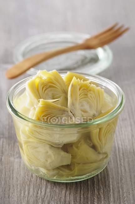 A jar of pickled artichoke hearts in glass jar over wooden surface — Stock Photo