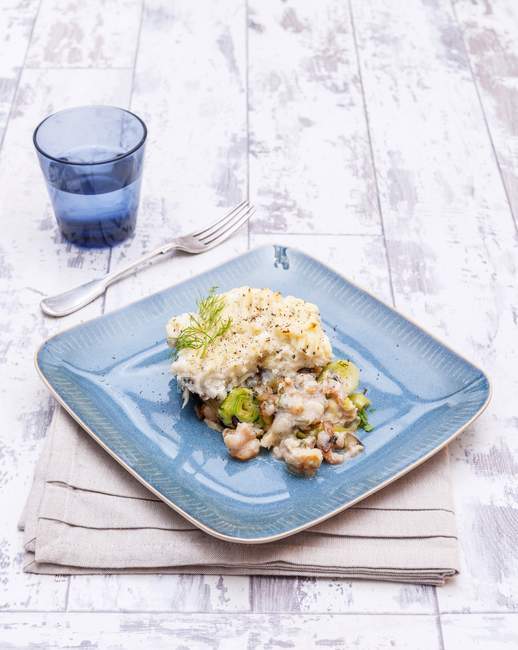 A portion of fish pie with prawns on blue plate over towel on wooden surface — Stock Photo