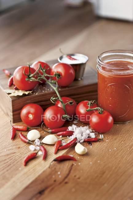 Salsa di pomodoro in un barattolo con ingredienti su superficie di legno — Foto stock