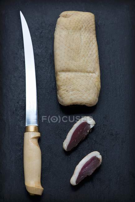 Копчена консервована качка з відрізаними скибочками поруч з ножем — стокове фото