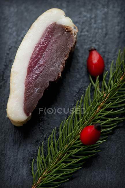 Closeup view of slice of smoked, marinated duck breast with a sprig of spruce and rose hips on a slate platter — Stock Photo