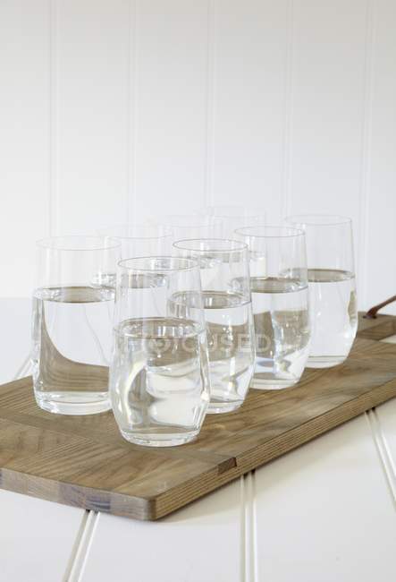 Water glasses on wooden chopping board — Stock Photo