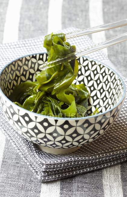 Elevated view of a patterned bowl of seaweed held with glass chopsticks — Stock Photo