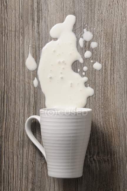Taza de leche derramada y taza volteada - foto de stock