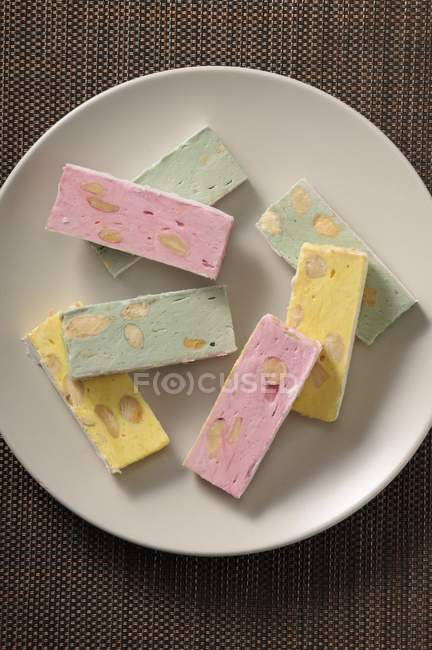 Nahaufnahme von oben pastellfarbene Turrons mit Nüssen auf weißem Teller — Stockfoto