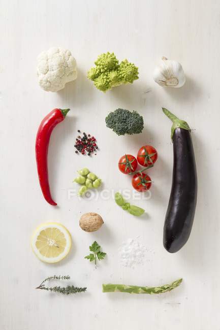 Varias verduras, especias y hierbas en una superficie blanca - foto de stock