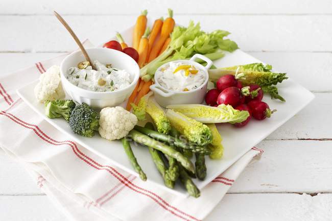 Raw vegetables with various dips  on white plate over towel — Stock Photo