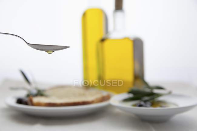 Aceite de oliva goteando de una cuchara sobre la mesa - foto de stock