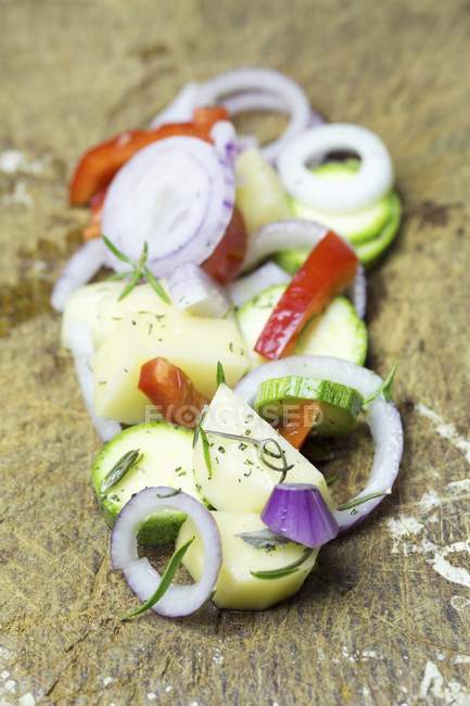 Onion rings, sliced potato, courgette slices and peppers on a wooden chopping board — Stock Photo