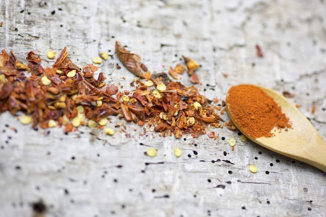 Closeup view of chilli powder on a wooden spoon and chilli flakes on a wooden surface — Stock Photo