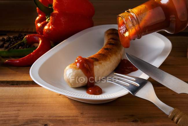 Sausage with ketchup and chili peppers — Stock Photo