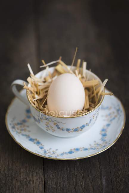 Fresh egg in teacup with straw — Stock Photo