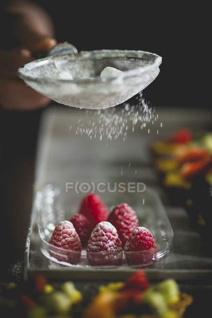 Closeup cropped view of hand dusting raspberries with icing sugar — Stock Photo