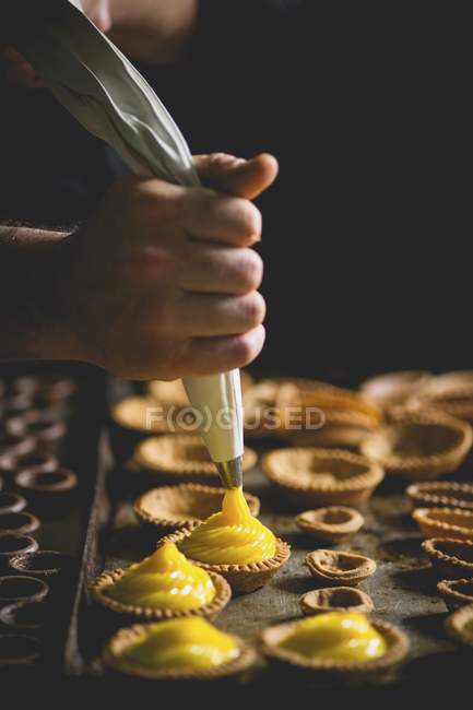 Shortcrust tartlets being filled with vanilla cream — Stock Photo
