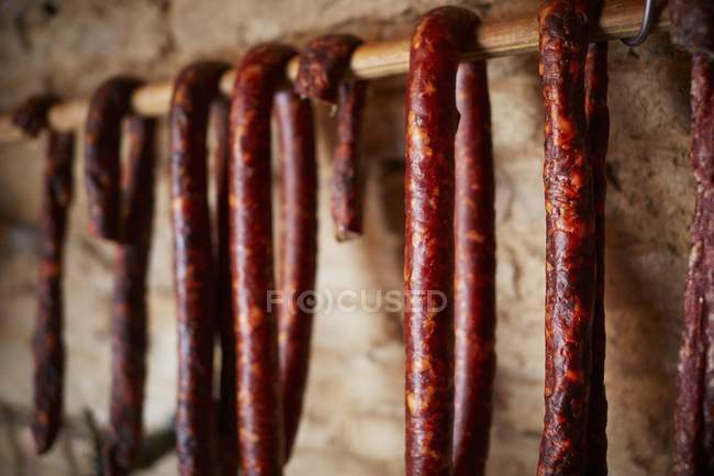 Air dried Salsiccia sausages hanging from a wooden bar — Stock Photo