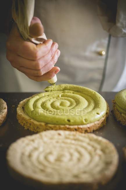 Cropped view of a confectioner piping pistachio cream on a sponge base — Stock Photo