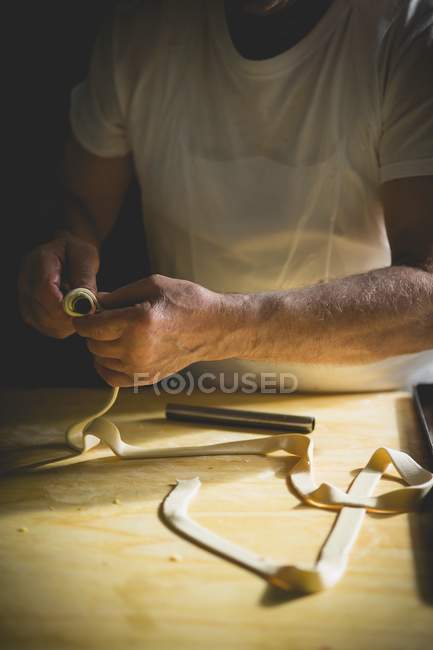 Обрезанный вид кондитера, катающего полоску теста вокруг металлической палки — стоковое фото