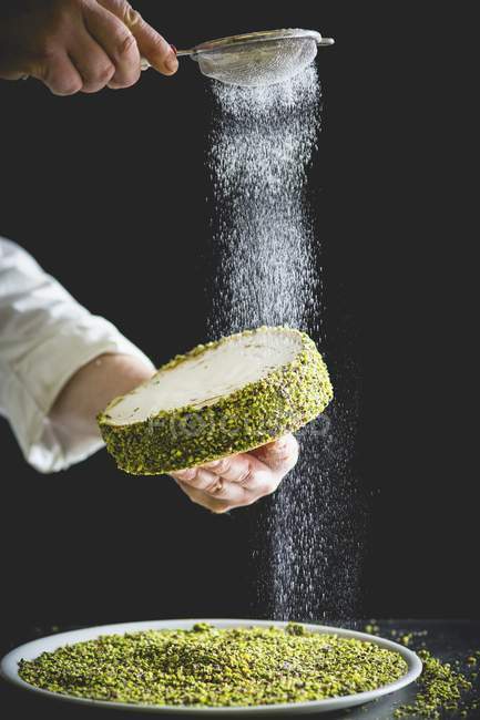 Confectioner dusting a small pistachio cake — Stock Photo