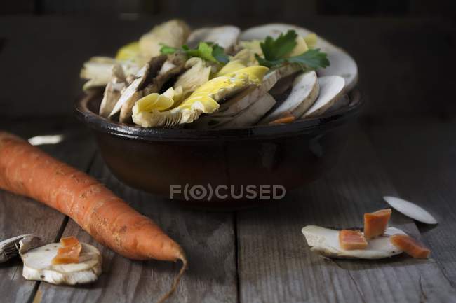 Cogumelos crus e fatiados em uma tigela em uma mesa de madeira — Fotografia de Stock