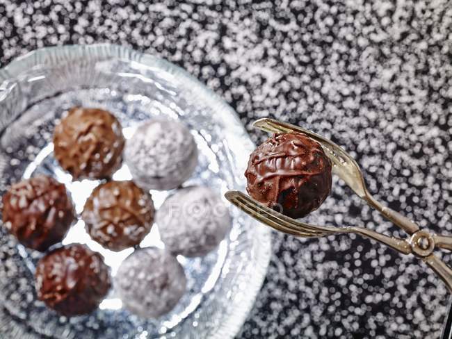 Vue rapprochée de pinces tenant praliné de truffe sur plaque de verre de diverses truffes — Photo de stock