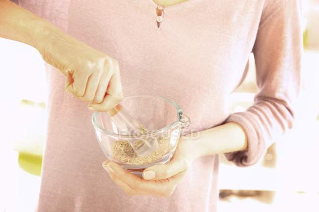 Cropped view of woman grounding nuts in glass mortar — Stock Photo