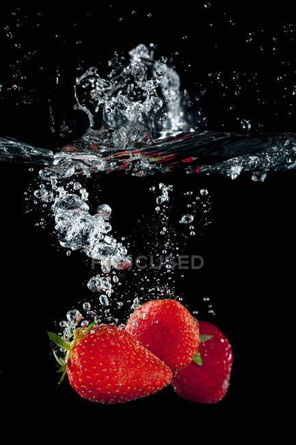 Fresas que caen en el agua - foto de stock
