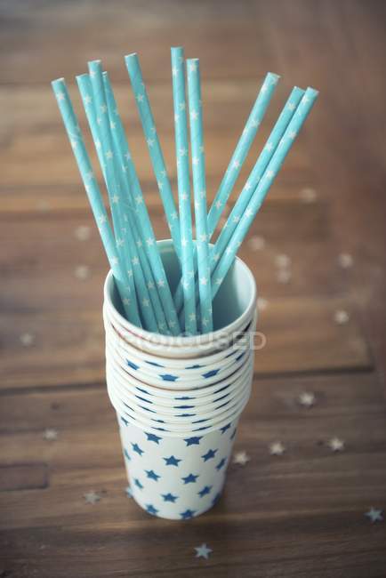 Vue rapprochée de pailles bleues dans une pile de tasses en papier décorées d'étoiles — Photo de stock